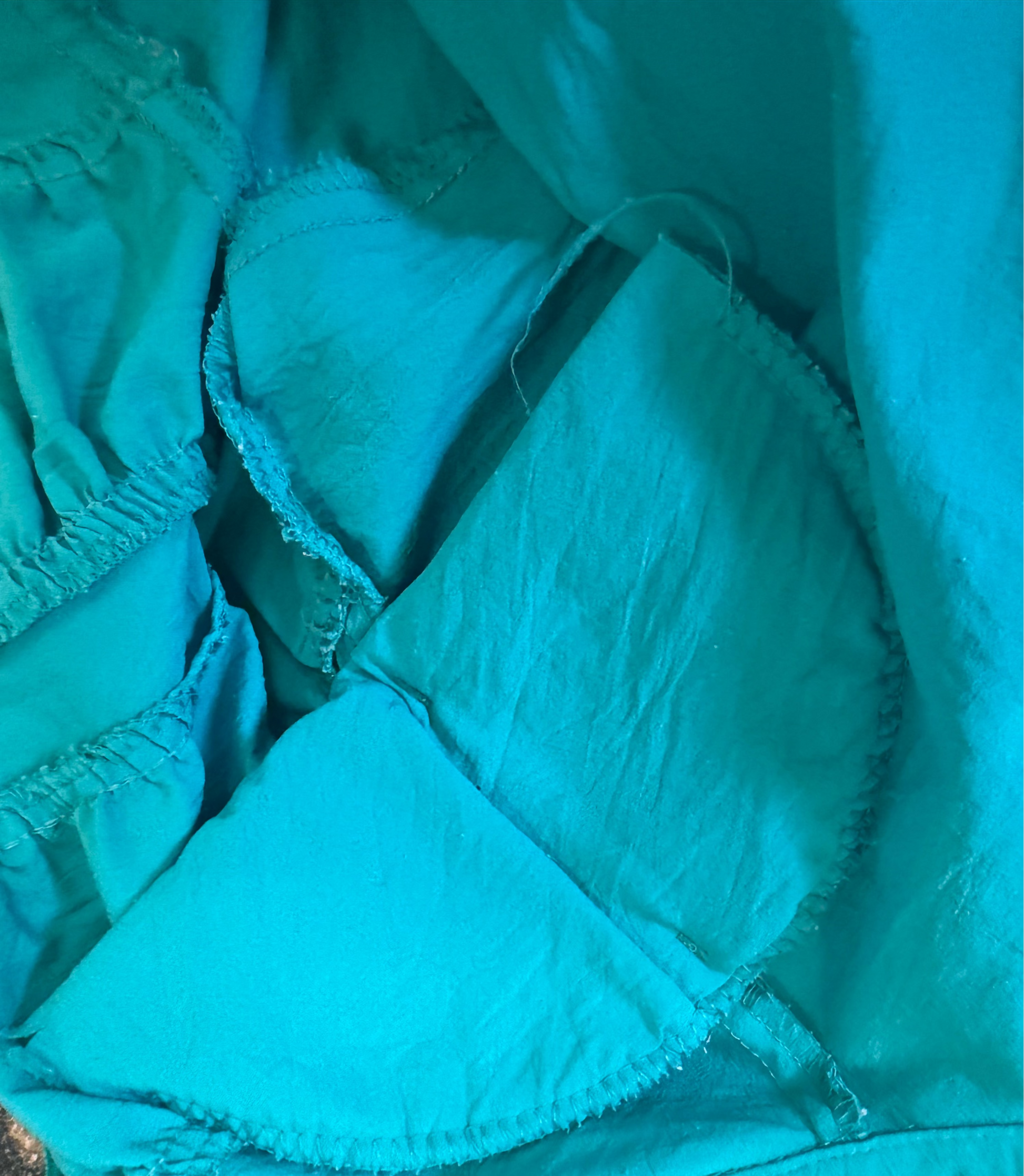 Close-up of a turquoise fabric with ruffled edges. Shoulder pad details. 
