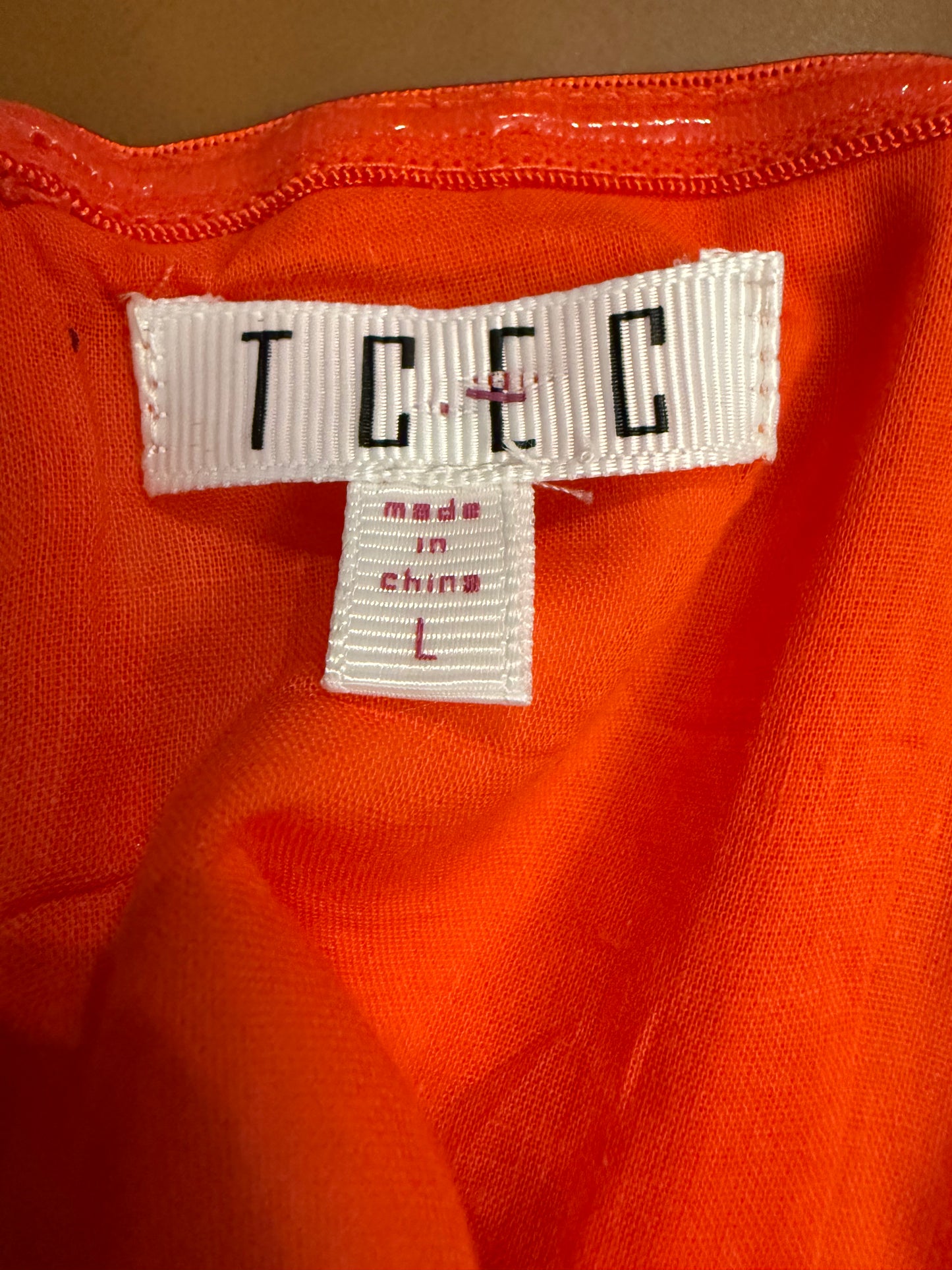 Close-up of an orange garment with a label displaying 'TECC' and 'Made in China L'.