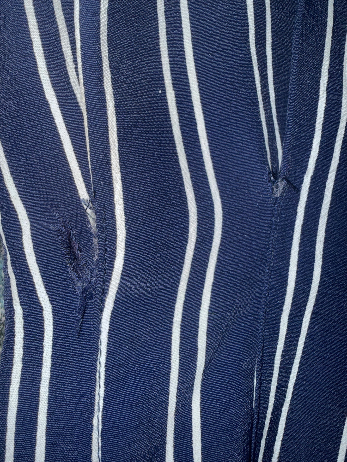 Close-up of blue and white striped fabric with visible stitching tear