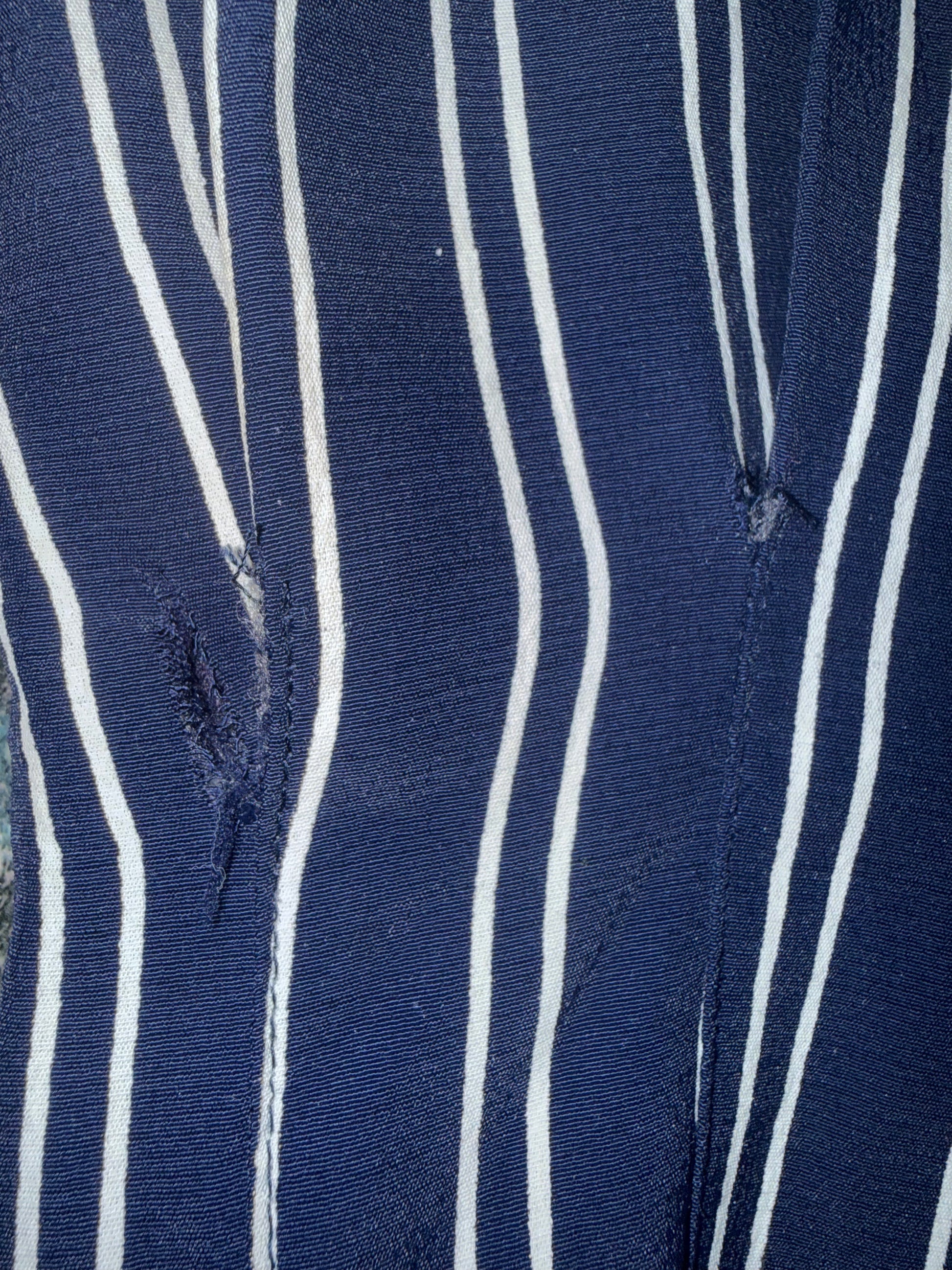 Close-up of blue and white striped fabric with visible stitching tear