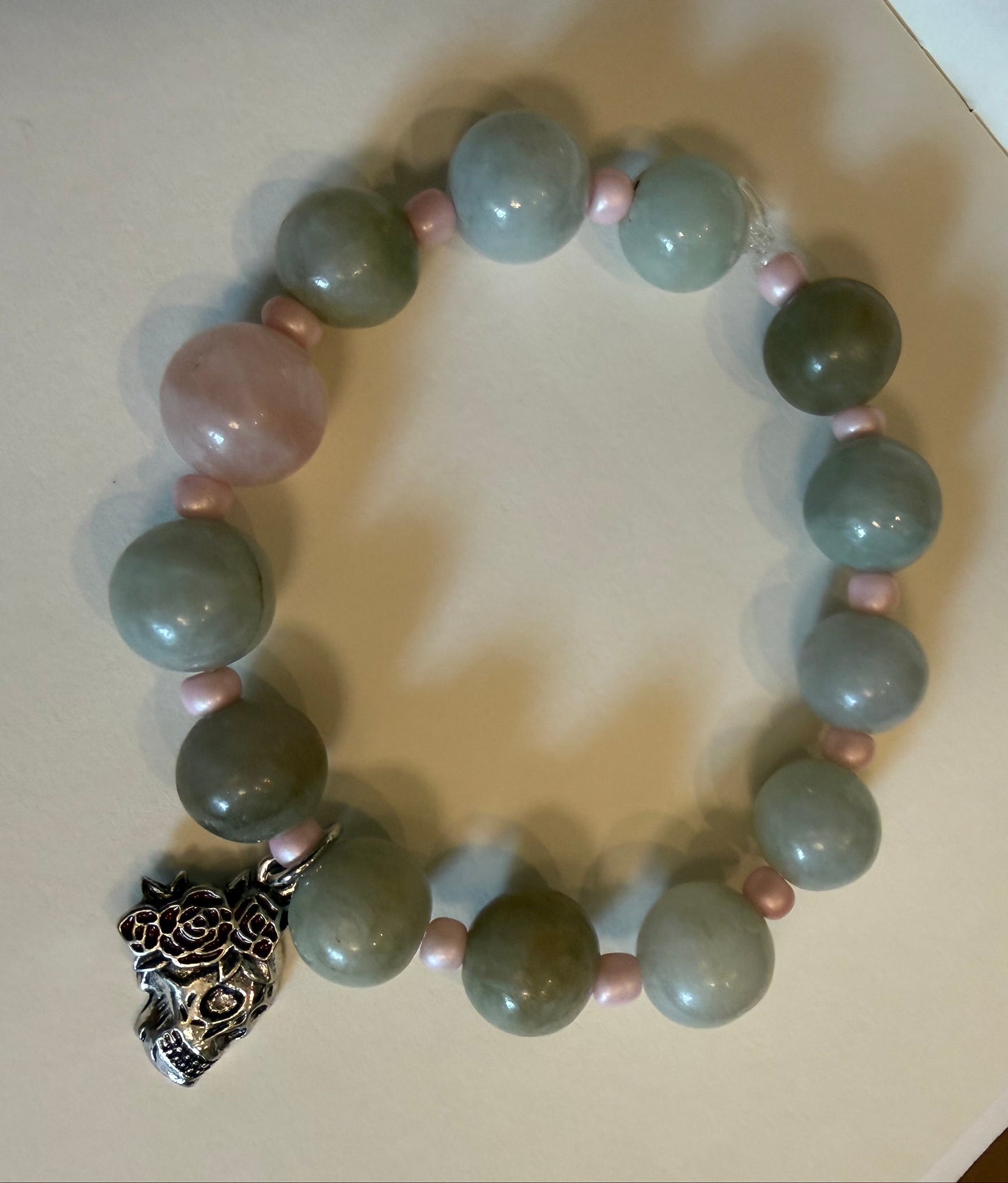 Bracelet with green and pink beads and a silver charm on a beige surface